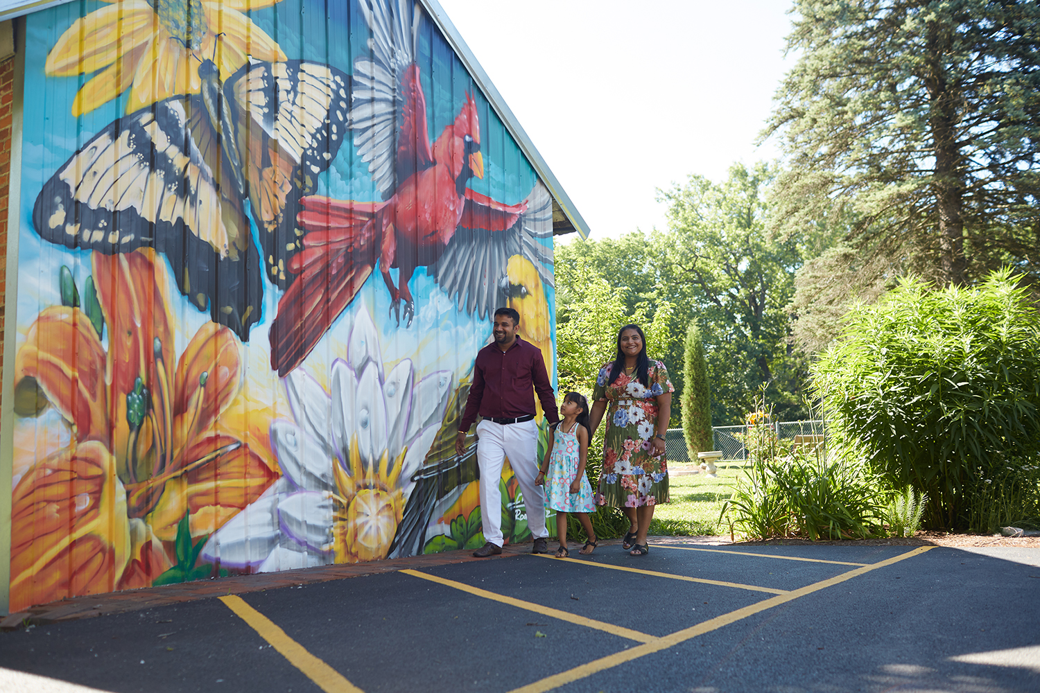 Three people walking next to a barn with art on it.