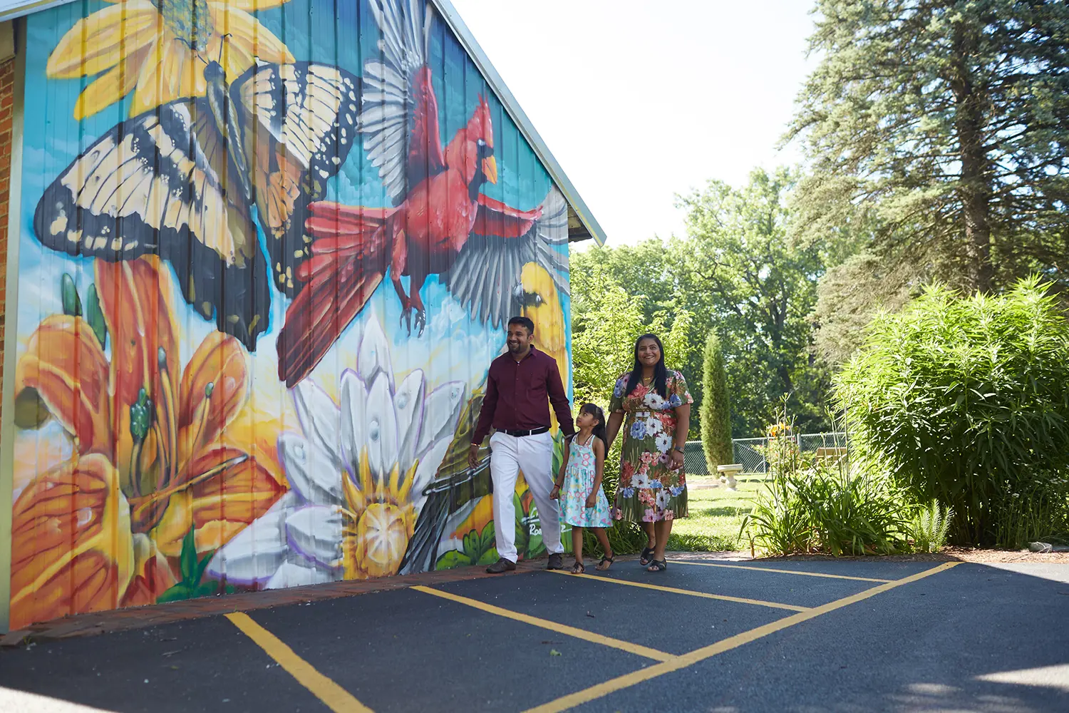 Three people walking next to a barn with art on it.